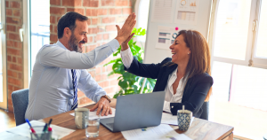 People sitting at an office desk smiling and high-fiving